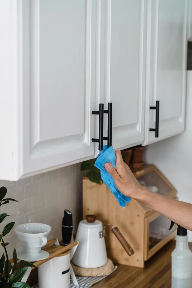 Cleaner wiping kitchen cabinet handles as part of a regular house cleaning service